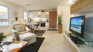 Een moderne woonkamer met een bank, een salontafel, een televisie en een keuken op de achtergrond.