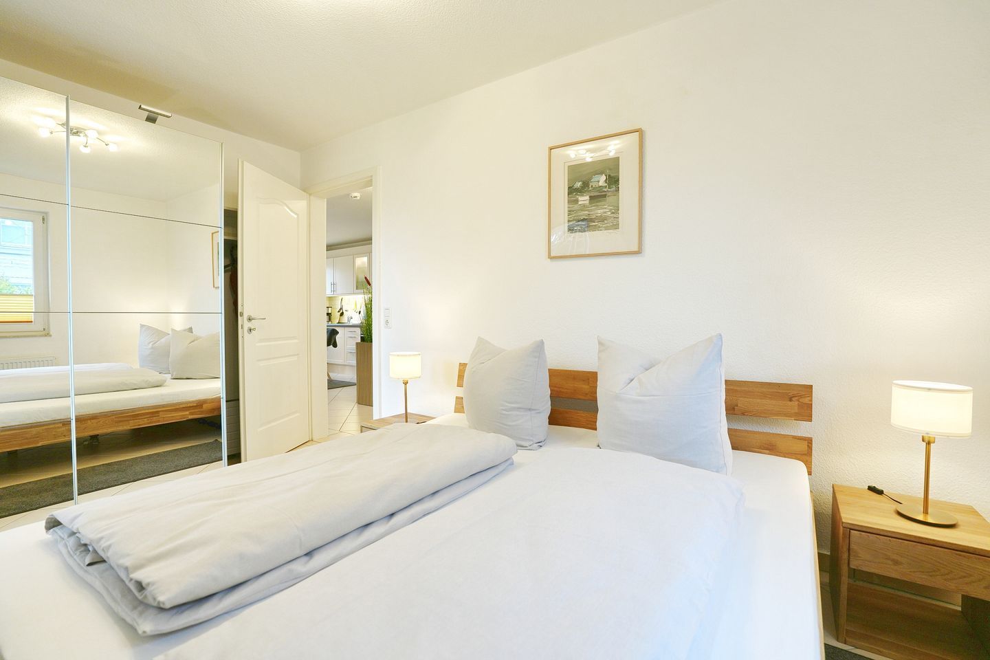 Une chambre d’hôtel avec un lit, des tables de chevet, un miroir, un tableau encadré au mur et une vue sur la chambre adjacente.