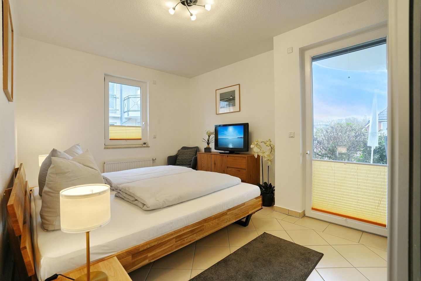 Une chambre à coucher avec un lit, une télévision, une fenêtre, un radiateur et un balcon.