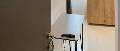 A room with a door labeled '502', a small table with a remote control, a wooden wardrobe, and a wall-mounted screen displaying various app icons.
