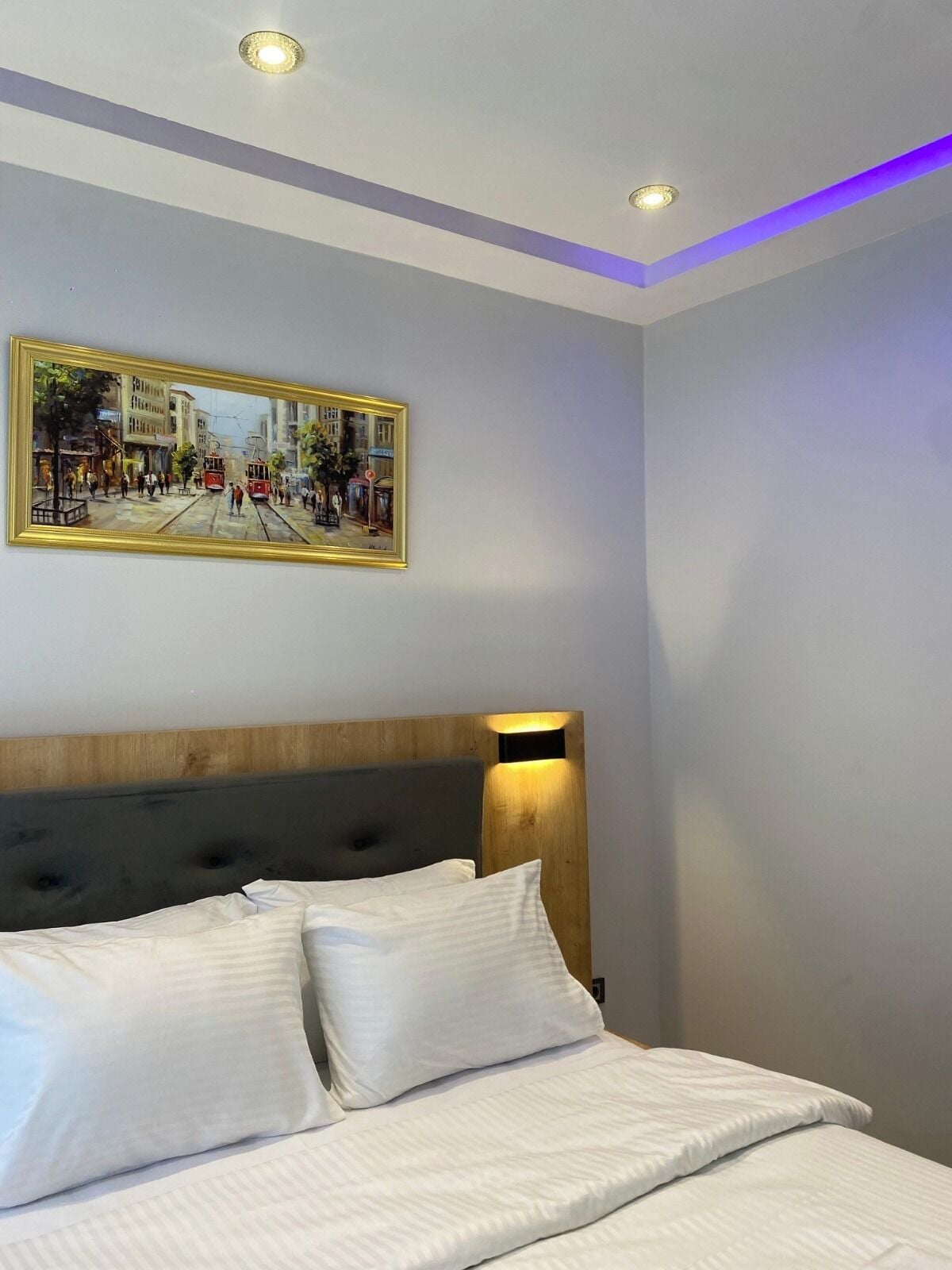Hotellihuone, jossa on sänky, sängynpääty, taulu ja upotetut kattovalaisimet.