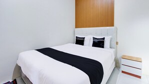 Un dormitorio con cama, un panel de pared de madera, un cabecero blanco y una mesita de noche con cajones.