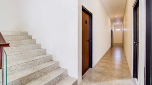 Un pasillo con una escalera que lleva a una puerta, suelo de baldosas y una pared lisa.