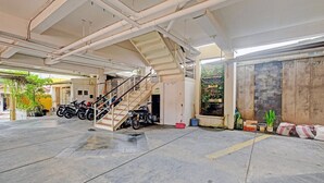 Ein überdachter Parkbereich mit einer Treppe zum Hauseingang, mehreren abgestellten Motorrädern und einem gefliesten Boden.