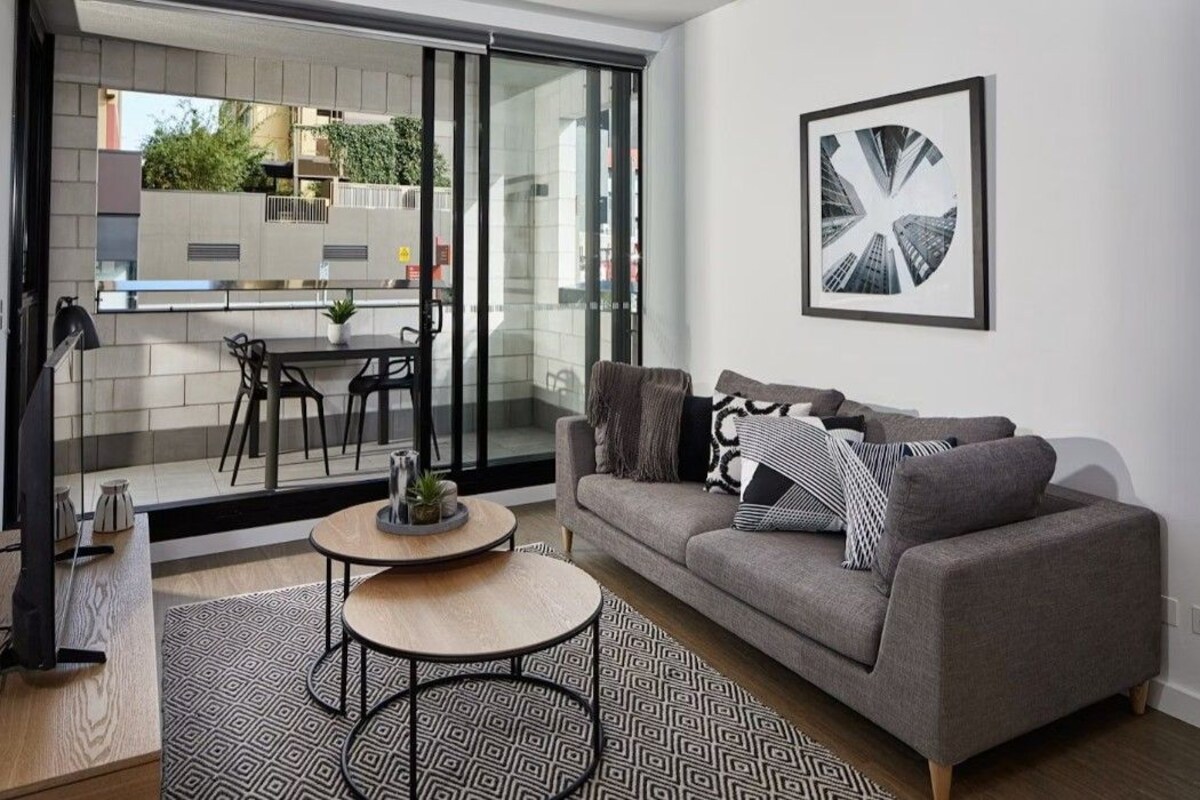A modern living room with a grey sofa, a round coffee table, and a large window with a view of a cityscape.