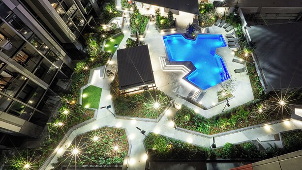 Vista aérea de un patio de hotel con piscina, rodeado de vegetación y senderos.
