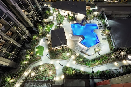An aerial view of a hotel courtyard with a swimming pool, surrounded by greenery and pathways.