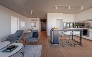 A modern kitchen with a central island, bar stools, and a dining area with chairs and a table. - Kingstreet Residences (Bowen Hills)