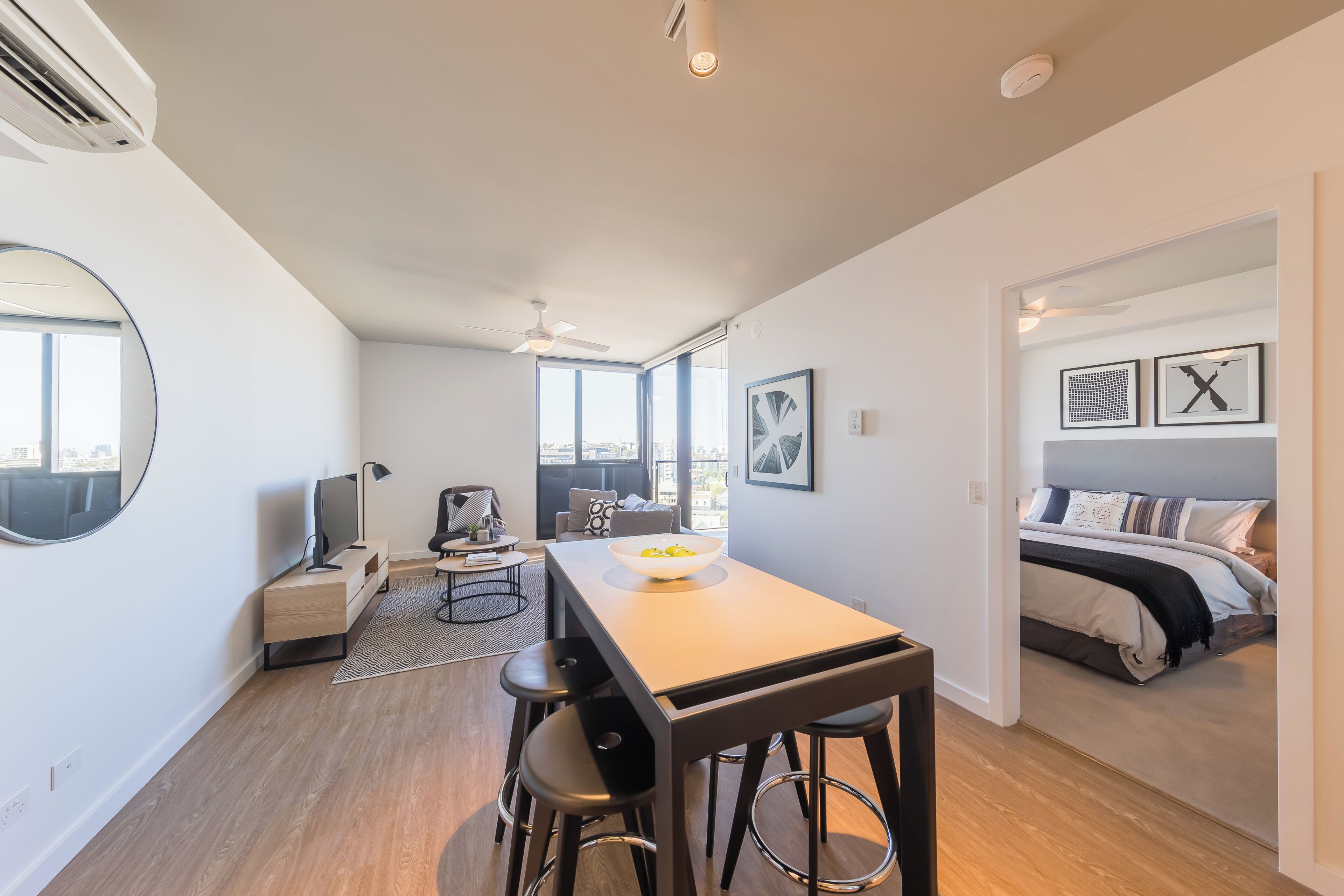 A modern, well-lit room with a dining table, bar stools, a TV, and a bed with a view.