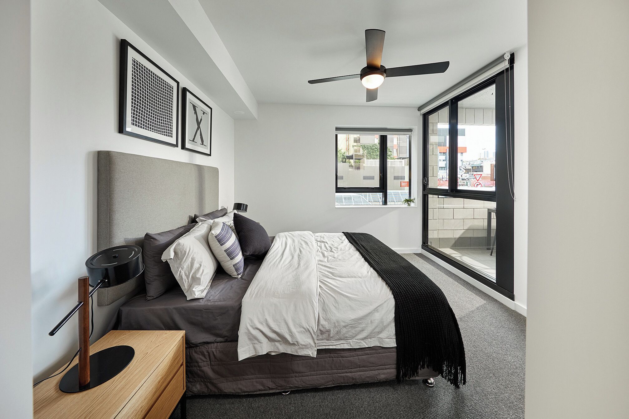 A modern bedroom with a bed, bedside table, lamp, and a large window.
