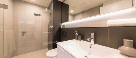 Une salle de bain moderne avec une douche à l’italienne en verre, un lavabo blanc et un grand miroir.