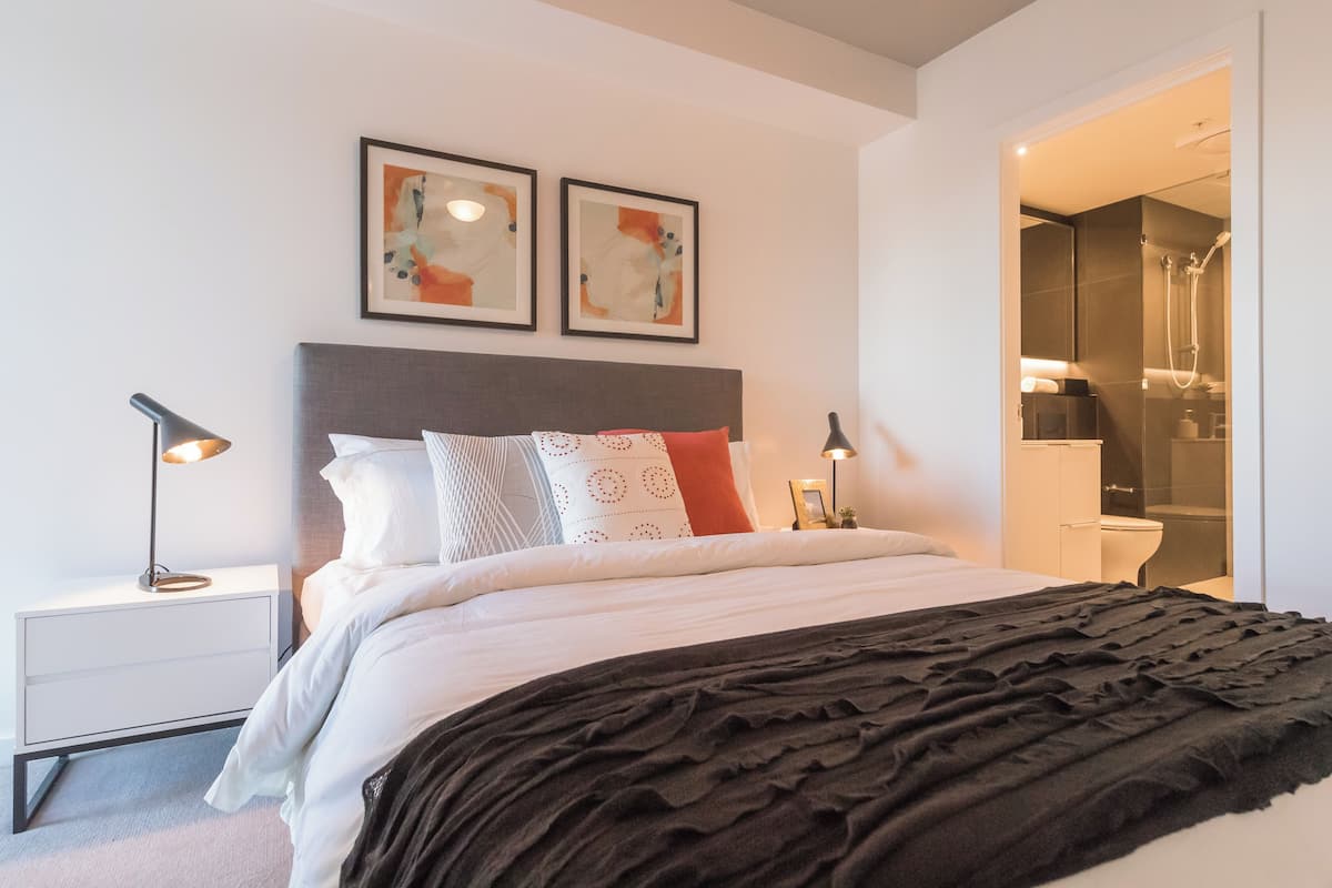 Un dormitorio moderno con una cama grande, mesitas de noche y un baño visible a través de una puerta abierta.