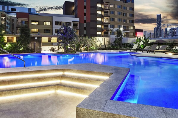A swimming pool with steps leading into it, surrounded by buildings and a sunset sky. - Kingstreet Residences (Bowen Hills)