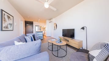 A modern living room with a sofa, coffee table, TV, and a ceiling fan.