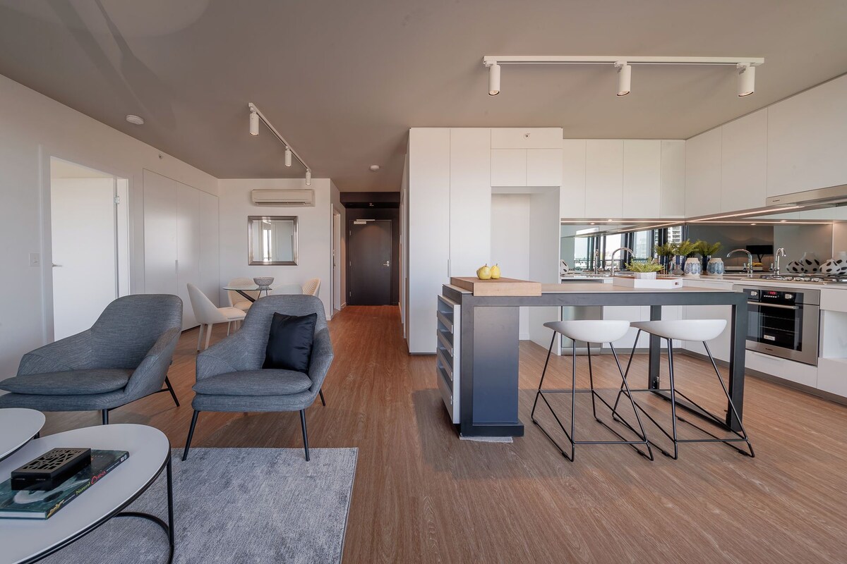 A modern kitchen with a central island, bar stools, and a dining area with chairs and a table.