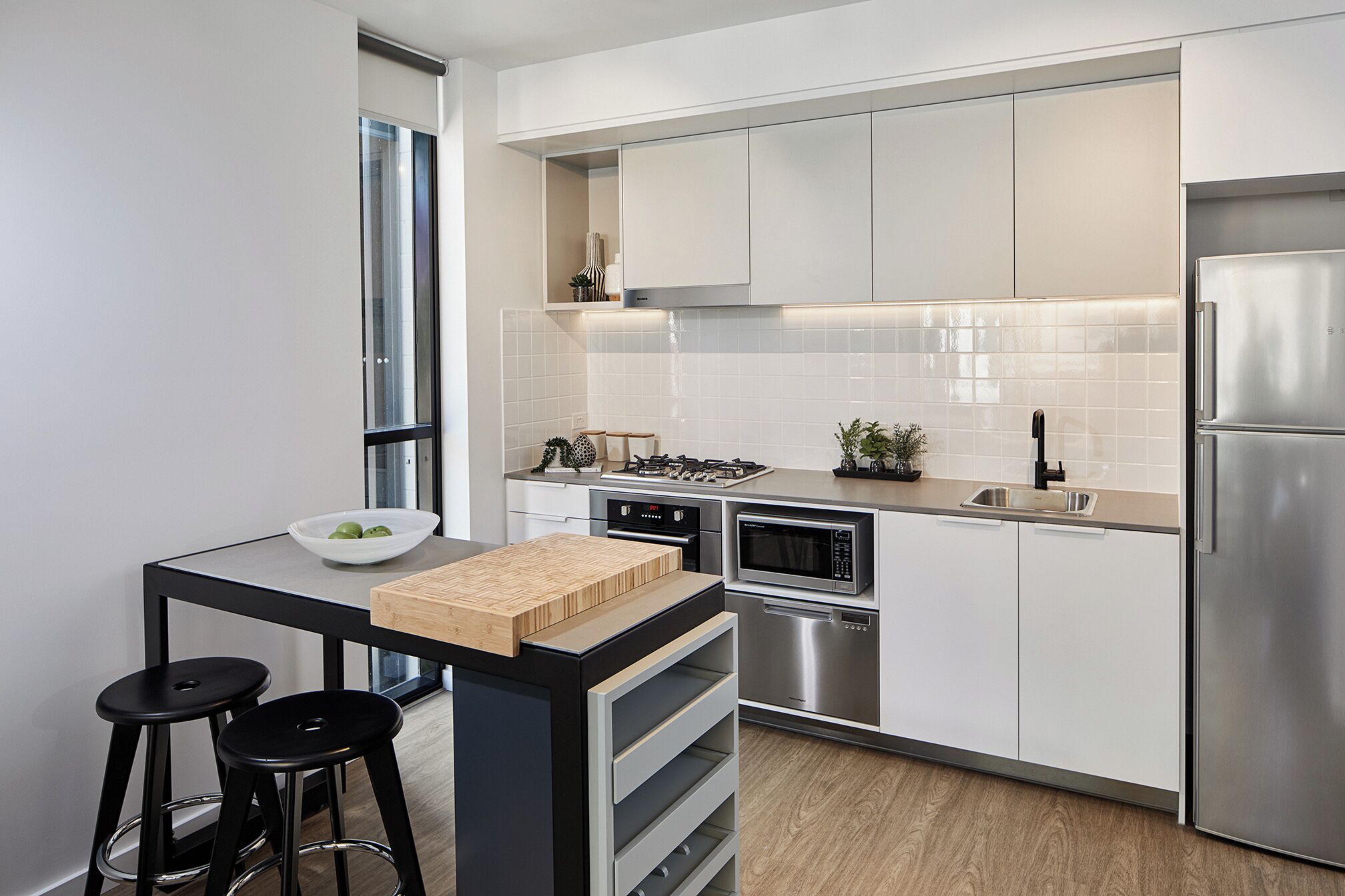 A modern kitchen with white cabinetry, stainless steel appliances, and a small island with stools.