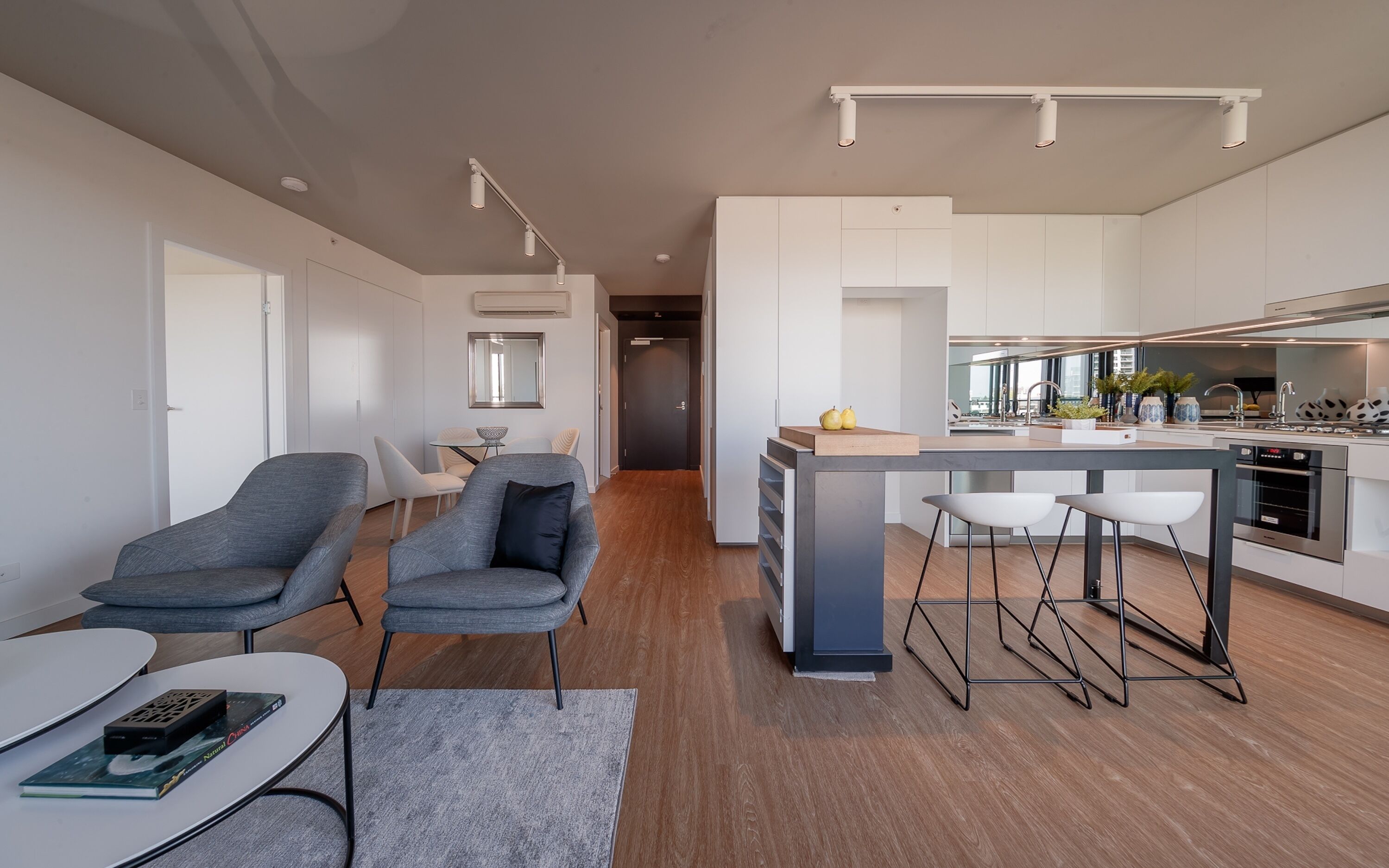 A modern kitchen with a central island, bar stools, and a dining area with chairs and a table.