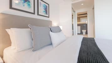 A neatly made bed with white linens and patterned pillows, a gray headboard, and two abstract art pieces on the wall.