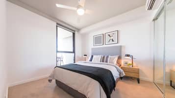 A bedroom with a bed, bedside tables, a ceiling fan, and a large window.