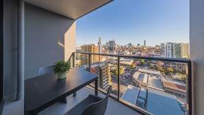 Un balcón con mesa y sillas, una planta en maceta y vista panorámica de la ciudad.