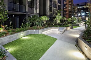 A landscaped outdoor area with a pathway, grass, and planters. - Kingstreet Residences (Bowen Hills)