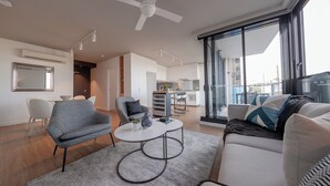 Una sala moderna con sofá, sillón y mesa de centro, un comedor con sillas, y una cocina al fondo.