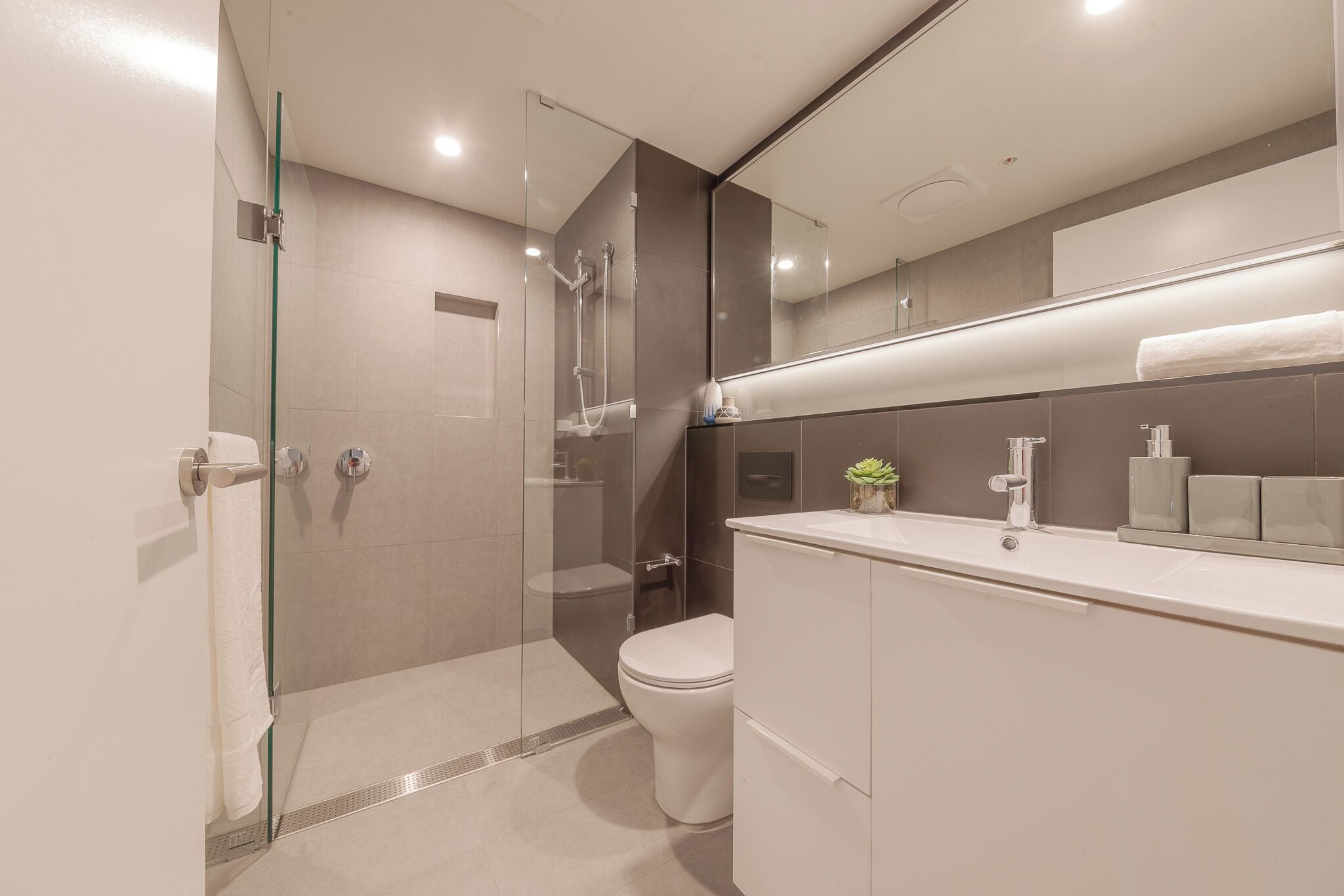 Une salle de bain moderne dotée d’une douche à parois de verre, de toilettes et d’un meuble-lavabo avec un miroir.