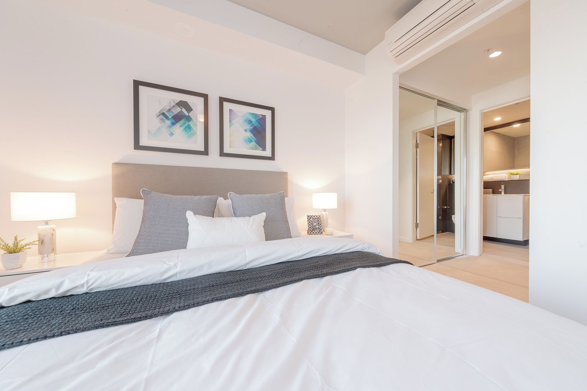 A modern hotel room with a large bed, bedside lamps, and abstract artwork on the wall.