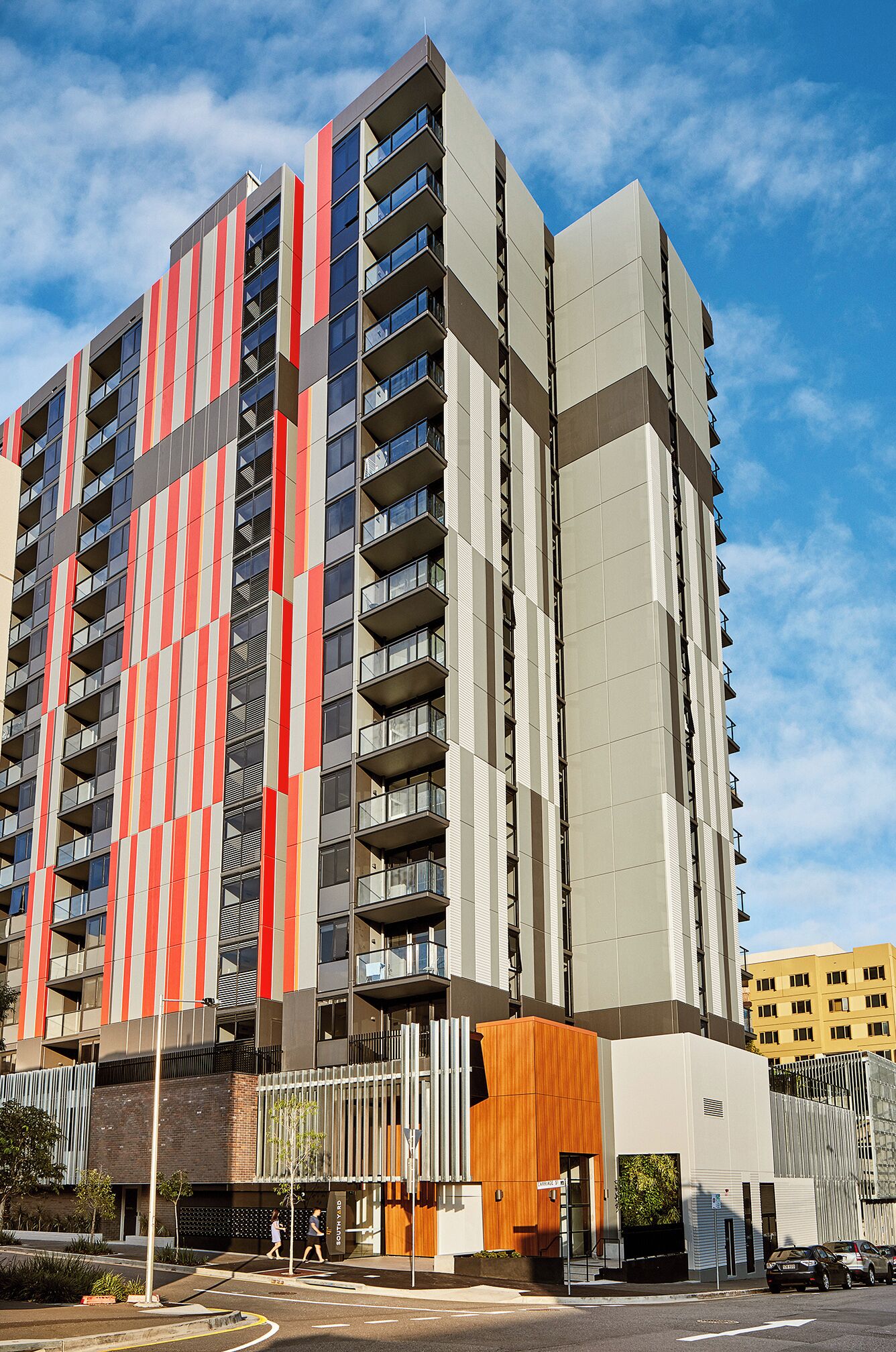 A modern high-rise building with a distinctive striped facade, multiple balconies, and a ground-level entrance with a wooden facade.