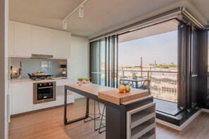 Una cocina moderna con una isla grande, horno empotrado y vistas a una obra a través de amplios ventanales.