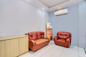 Ein Zimmer mit zwei Ledersofas, einem Holzschrank, einer Wand-Klimaanlage und einem vertikalen Banner.
