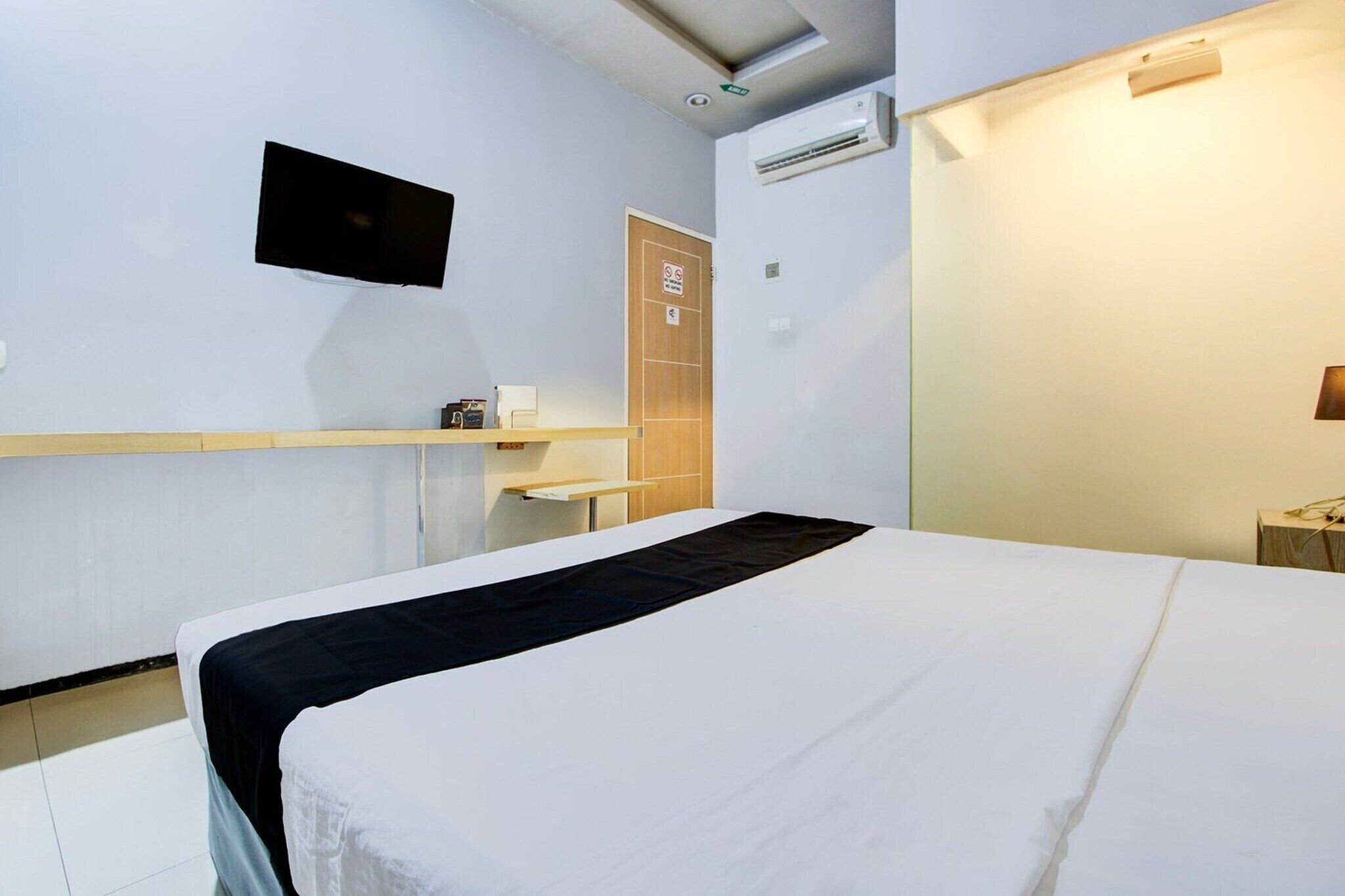 Une chambre d’hôtel équipée d’un lit, d’un téléviseur fixé au mur, d’un appareil de climatisation et d’une porte en bois.