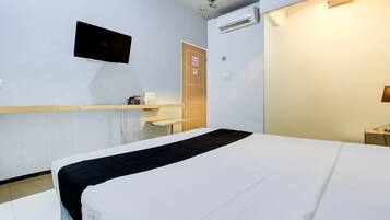 A hotel room with a bed, a mounted TV, an air conditioning unit, and a wooden door.