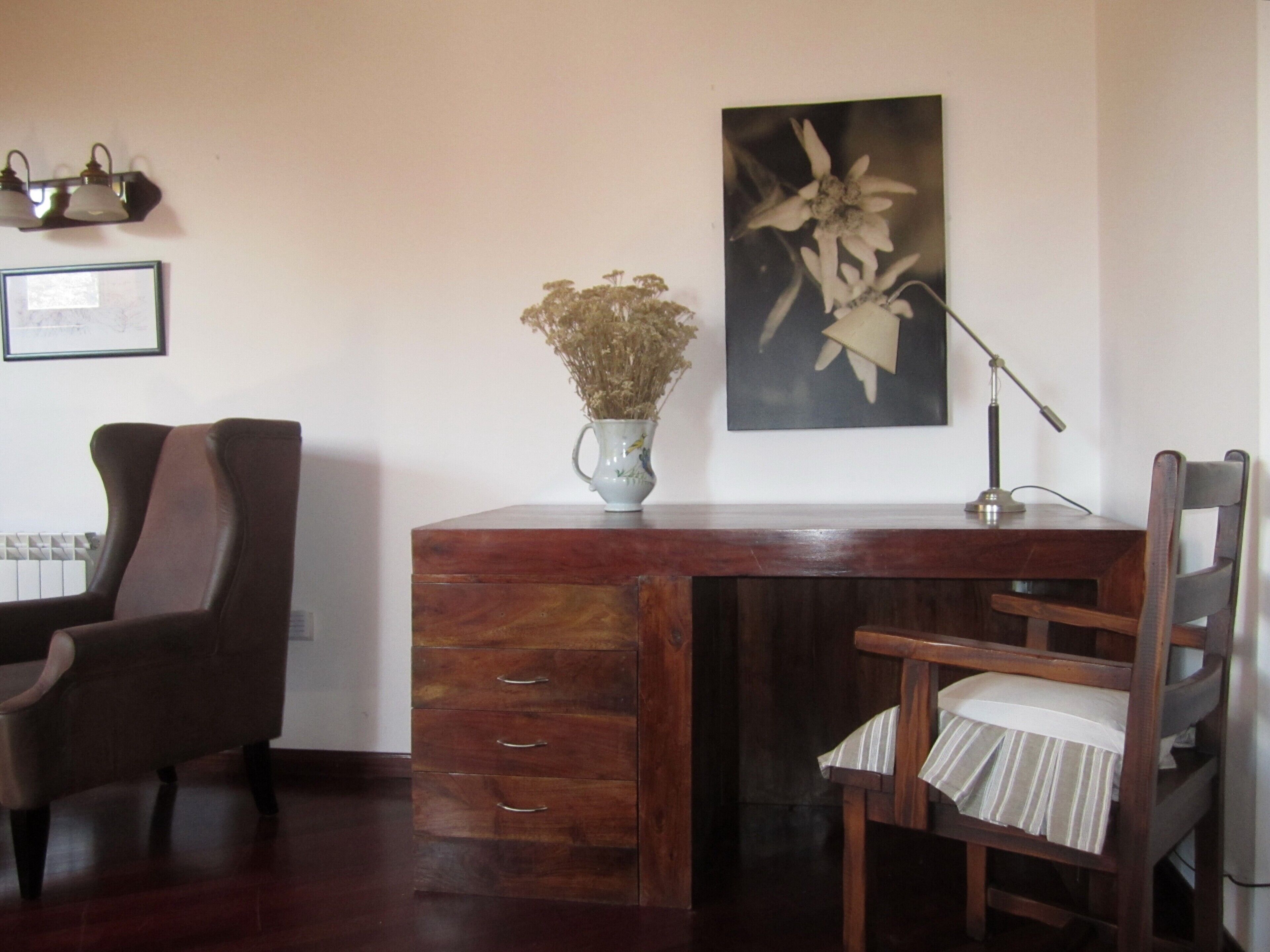 Un bureau en bois, orné d’un vase de fleurs séchées, d’une lampe et d’une chaise avec un coussin à rayures.