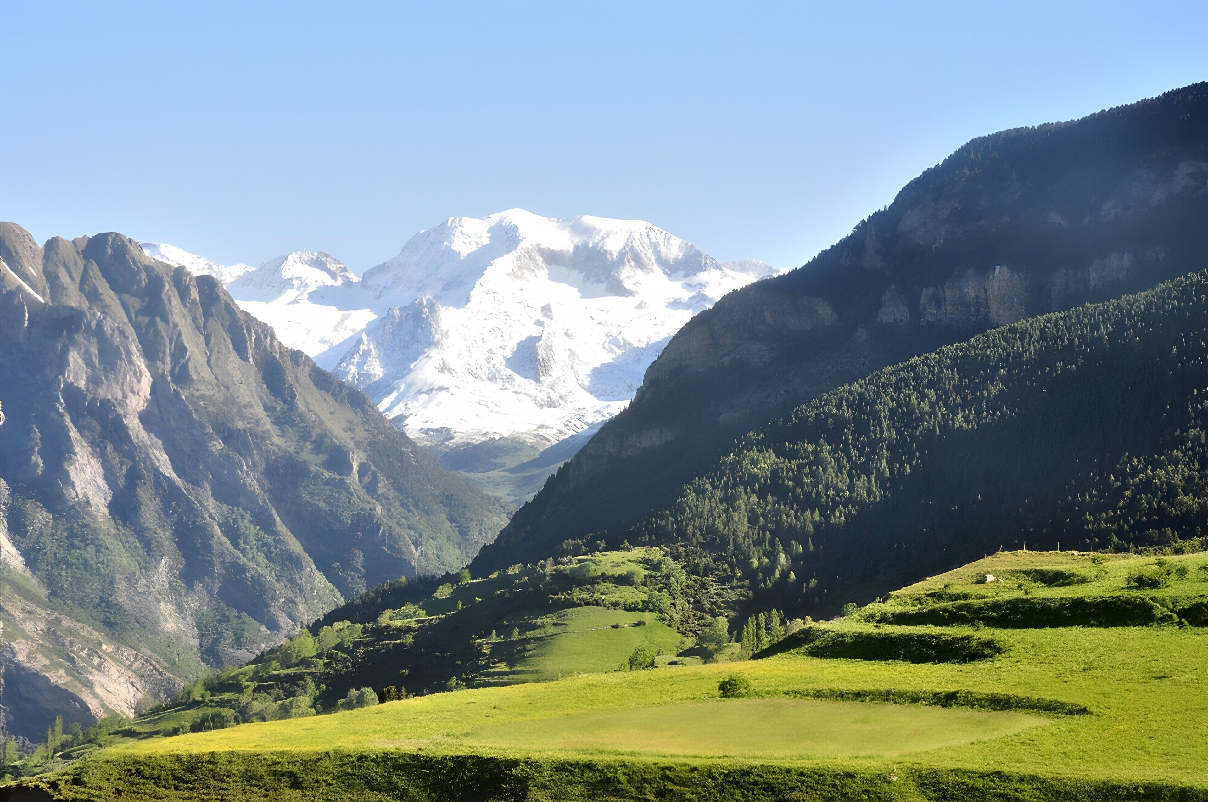 A mountainous landscape with snow-capped peaks, green valleys, and a clear sky.