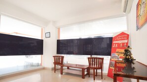 Une pièce avec une grande fenêtre, une table en bois et deux chaises, ainsi qu’une affiche rouge contenant des informations.
