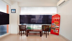 Une pièce avec une grande fenêtre, deux chaises en bois, une petite table et une affiche rouge contenant des informations.