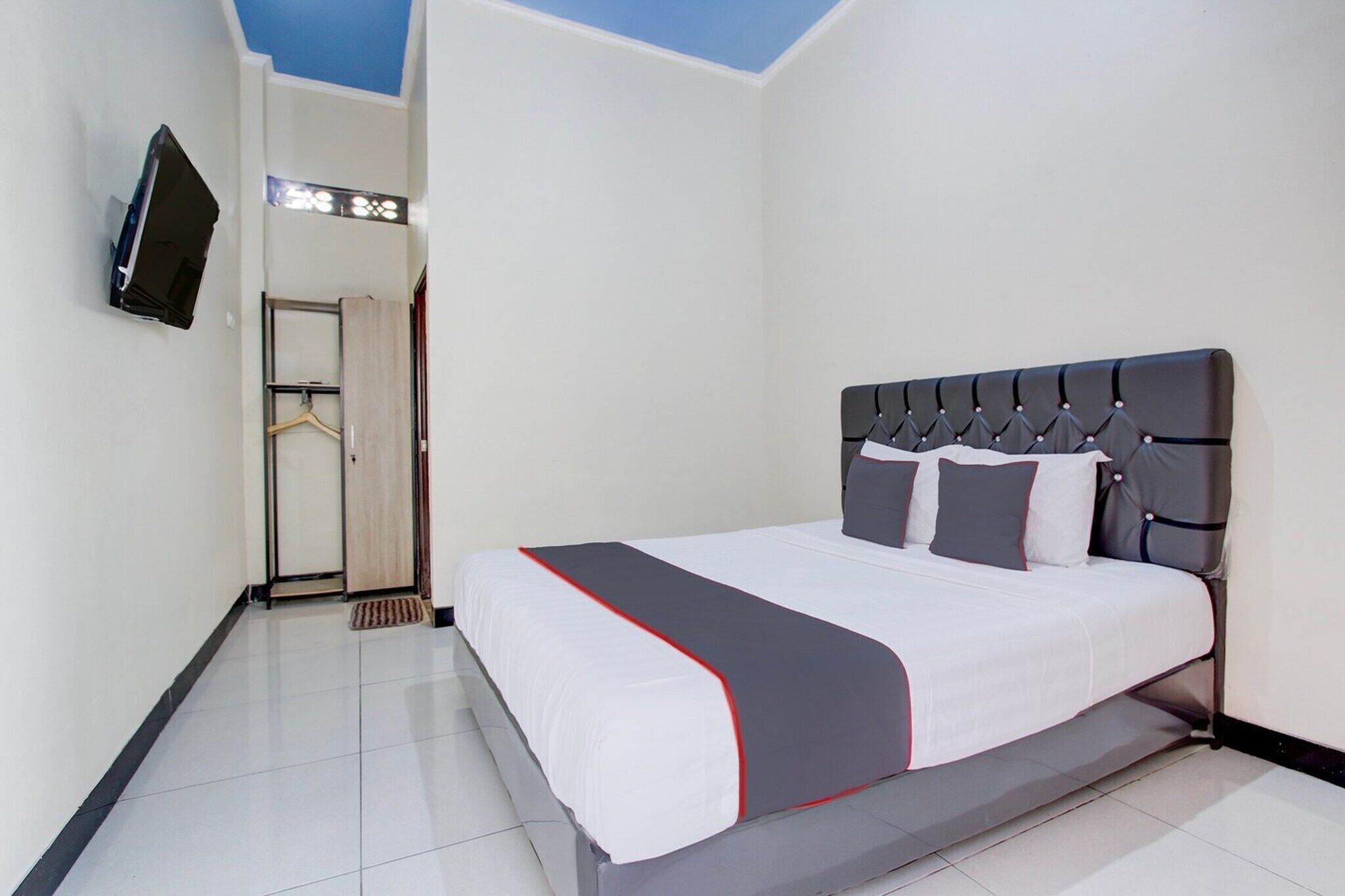 Ein Hotelzimmer mit einem Bett, einem an der Wand montierten Fernseher und einer Tür zu einem Flur.
