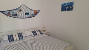 En snyggt bäddad säng med randiga sängkläder, ett nattduksbord med en lampa och en väggdekoration i blått och vitt.