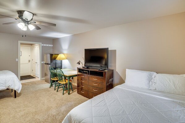 A hotel room with a bed, a desk with a chair, a television, a ceiling fan, and a door leading to another room. - Walkable Lake Escape! Elkhart Lake Condo (Elkhart Lake)