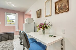 A modern room with a white desk, blue chair, and a vase with flowers. There is a window with a view of trees, a white air conditioner, and a gray cabinet. - Explore ATL! Cozy Couple's Hideaway in Ellenwood (Ellenwood)