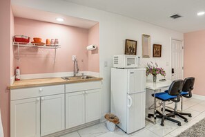 A kitchen with white cabinets, a sink, a microwave, and a refrigerator. There are two chairs and a trash can. - Explore ATL! Cozy Couple's Hideaway in Ellenwood (Ellenwood)
