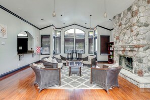 A spacious living room with wicker furniture, a stone fireplace, and large windows. - Spacious Patio + Modern Interior: Corona Escape! (Corona)