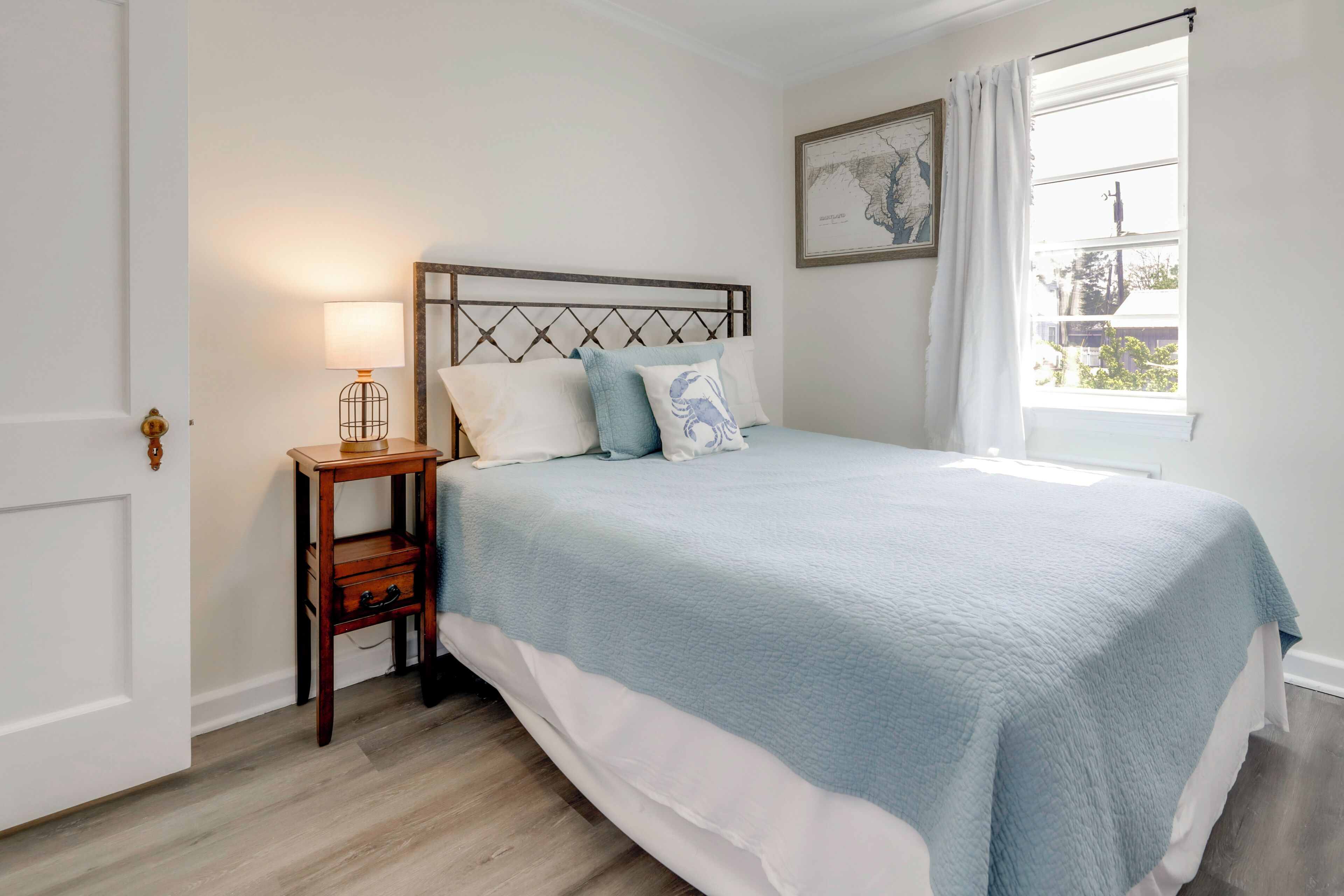 Een slaapkamer met een bed, nachtkastje, lamp en een raam met gordijnen.