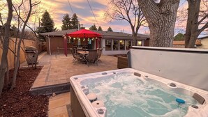 Ein Whirlpool in einem Garten mit Terrasse, einem roten Sonnenschirm und einem Ziegelhaus im Hintergrund.
