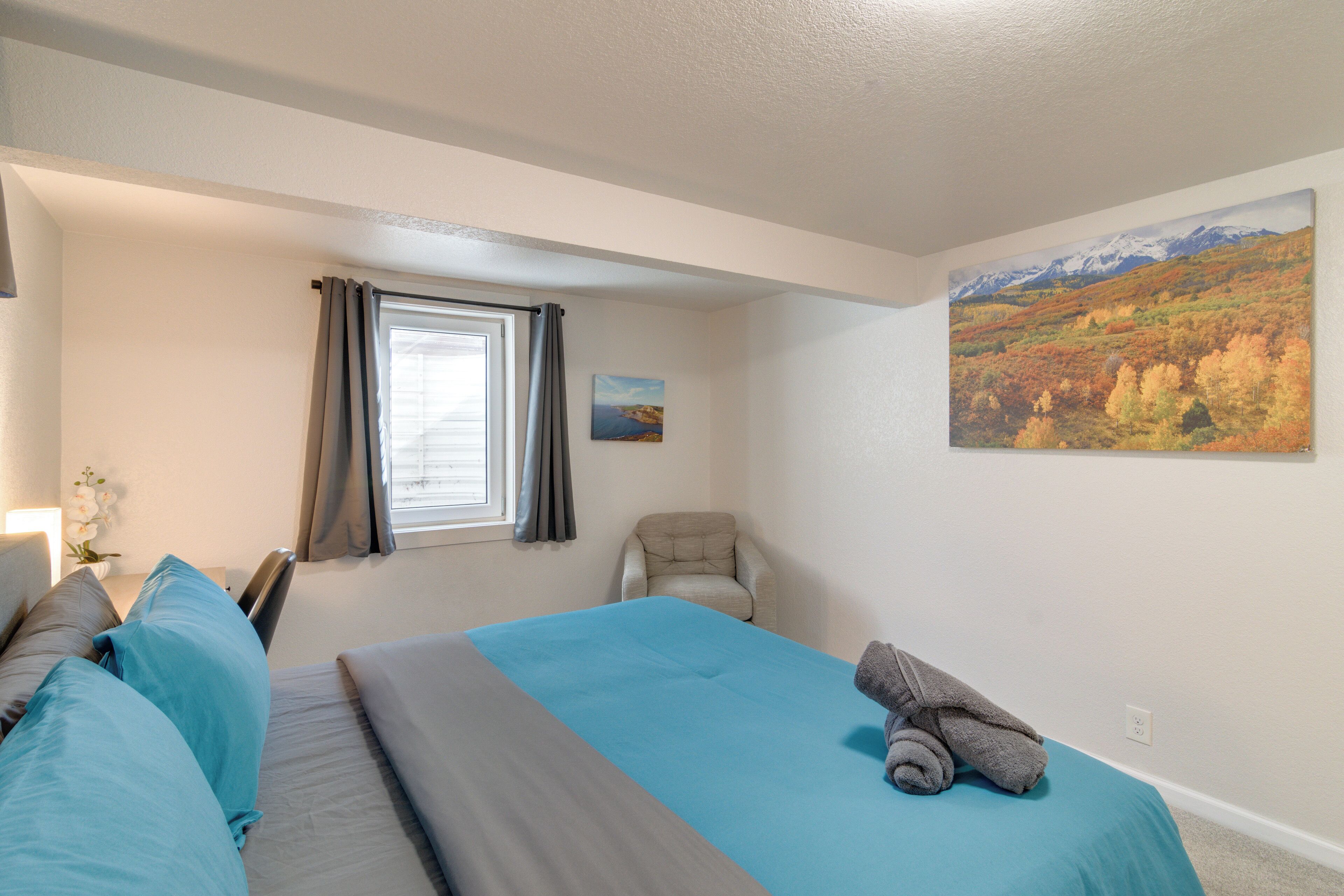 A bedroom with a bed, a chair, a window with curtains, and a painting on the wall.