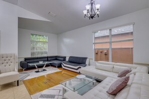 Ein Wohnzimmer mit Ecksofa, Glastisch, einem mit Stoff bezogenen Sessel und einer Chandelier.