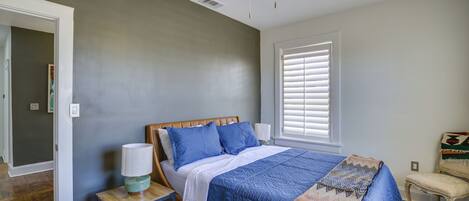 A bedroom with a bed, a nightstand, a chair, a ceiling fan, and a window with blinds.