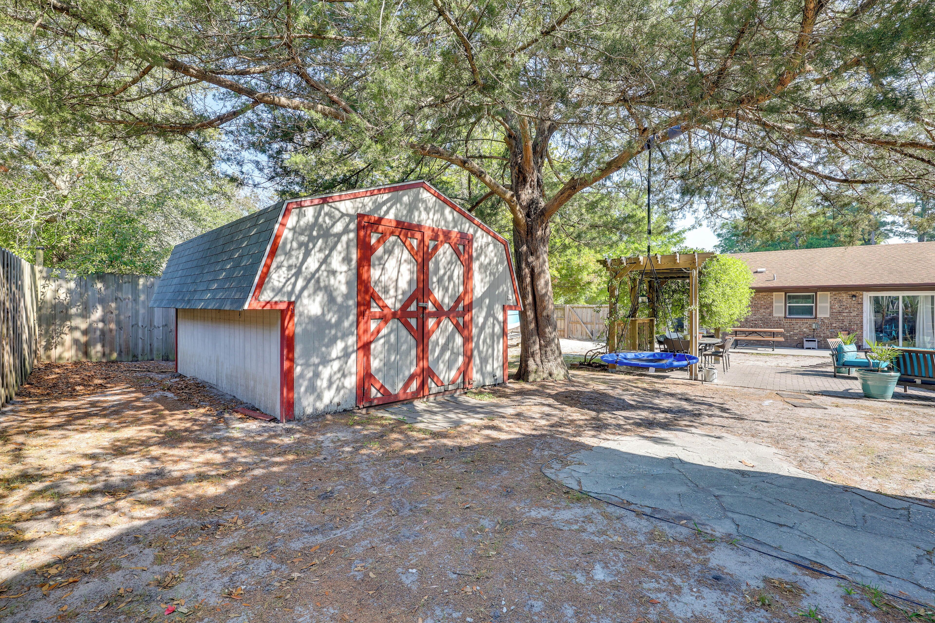 Une cour arrière clôturée avec un petit abri de jardin, un arbre et un espace patio aménagé avec du mobilier d’extérieur.