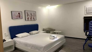 Una habitación de hotel moderna con una cama grande, una mesita de noche, una silla, una pequeña mesa redonda y dos cuadros en la pared.